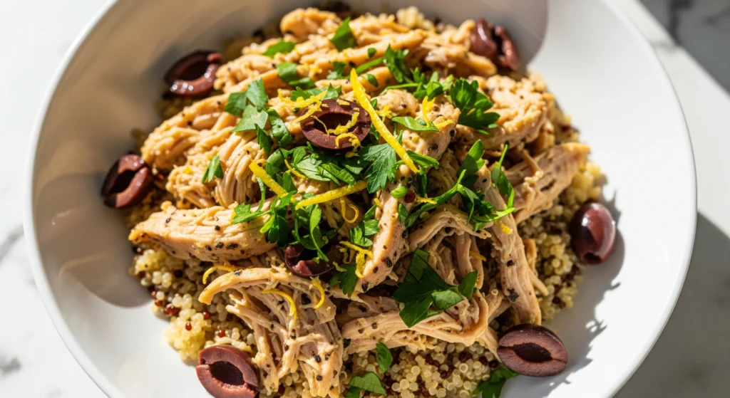 Healthy Mediterranean crockpot chicken served over quinoa, garnished with parsley and lemon. Perfect for dinner or clean meal prep.